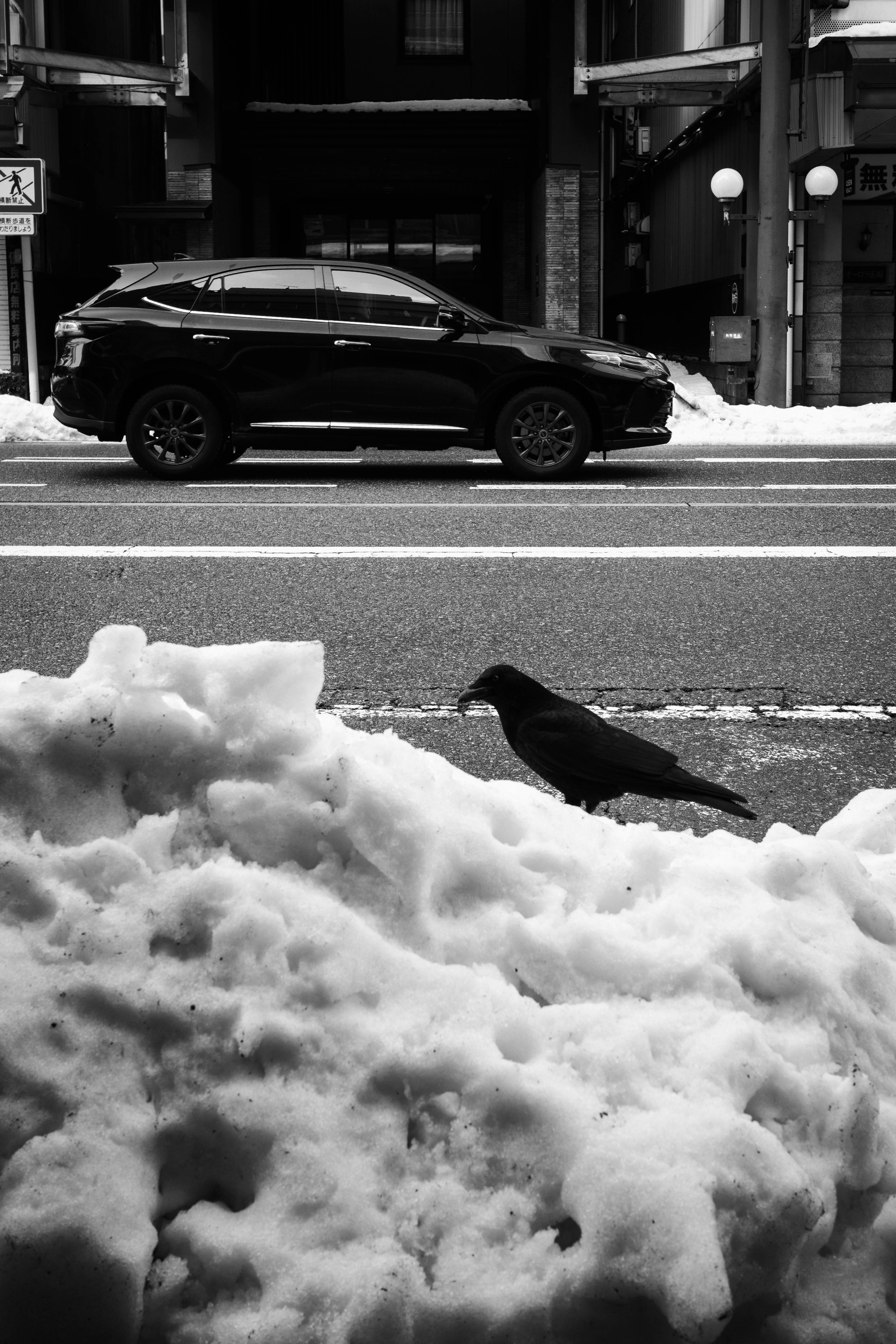 雪の歩道に積もった泡状の雪と黒い車のある路地