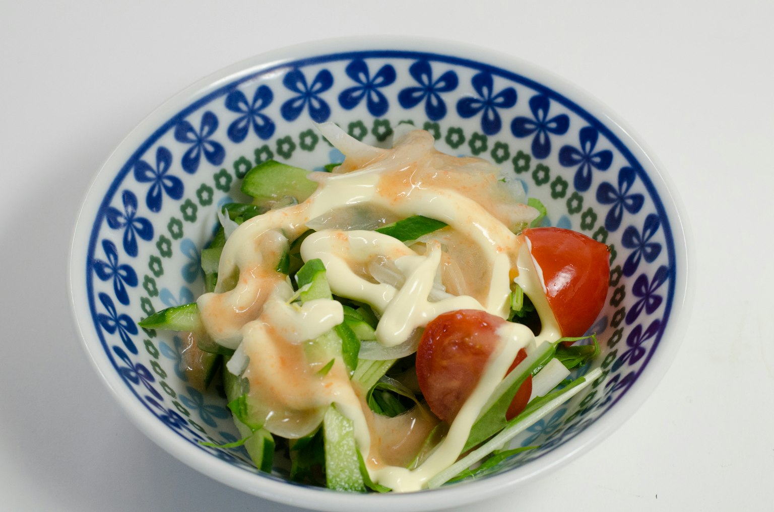 Salad with sliced vegetables and cherry tomatoes drizzled with mayonnaise in a blue floral bowl