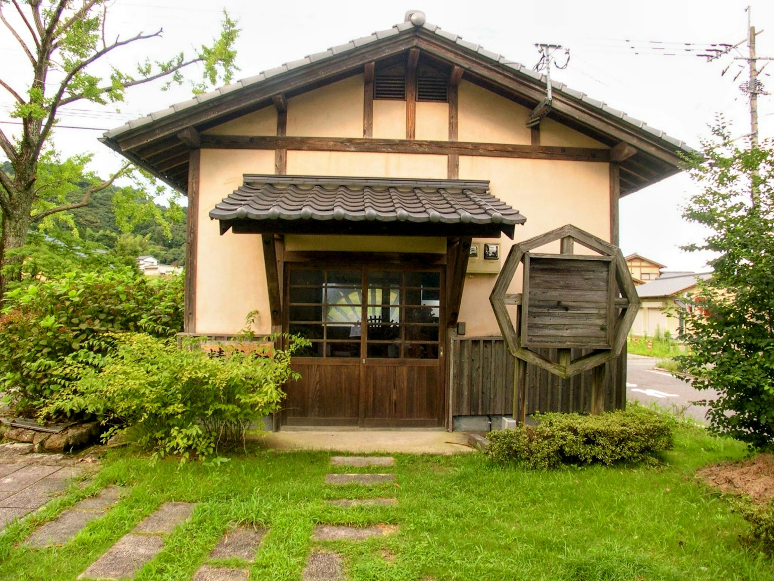 传统日本房屋，特点是木制门和屋顶，四周环绕着郁郁葱葱的绿树