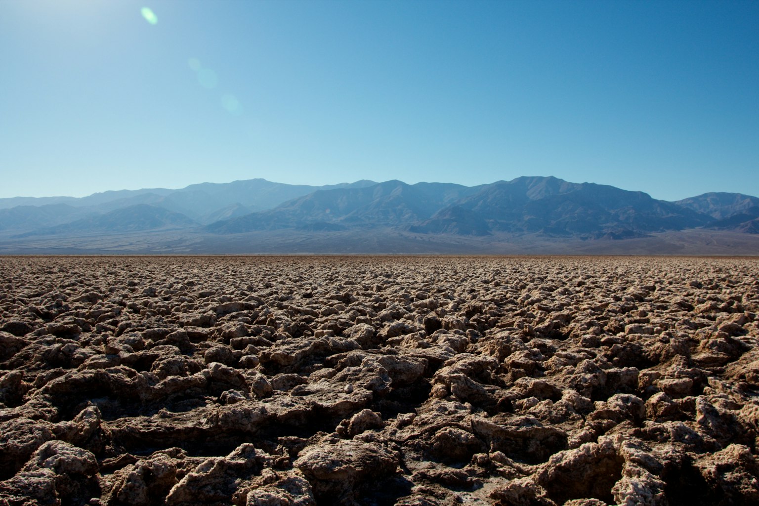 Paesaggio desolato con terreno screpolato e montagne lontane sotto un cielo blu