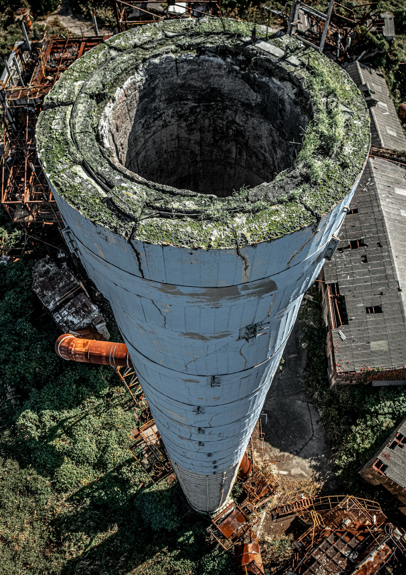 廃墟の中にある巨大な煙突の上からの視点 緑の苔が生えた円形の開口部 周囲には錆びた構造物が見える