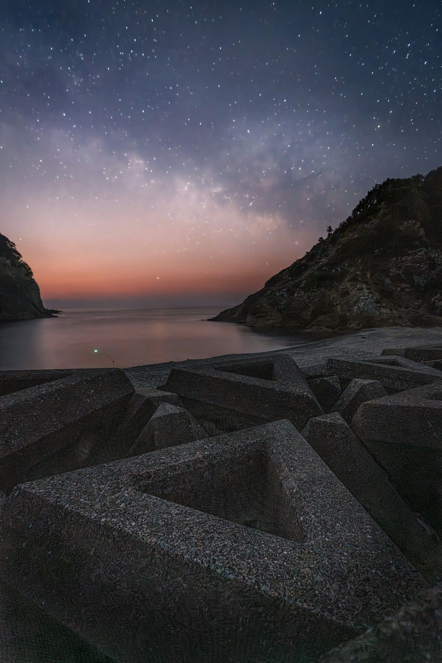 Starry night sky over a serene ocean view with triangular concrete structures in the foreground