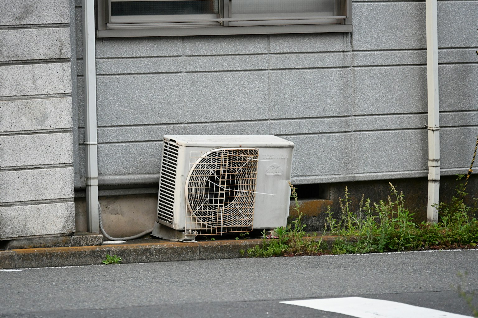 White air conditioning unit installed near a window surrounded by grass