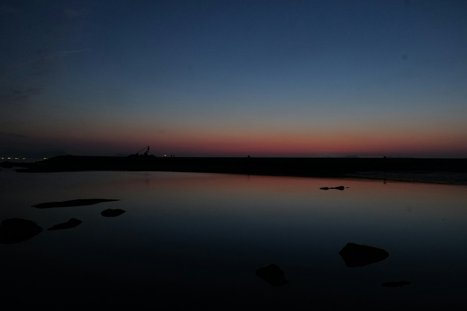 Agua tranquila reflejando tonos del amanecer con horizonte oscuro