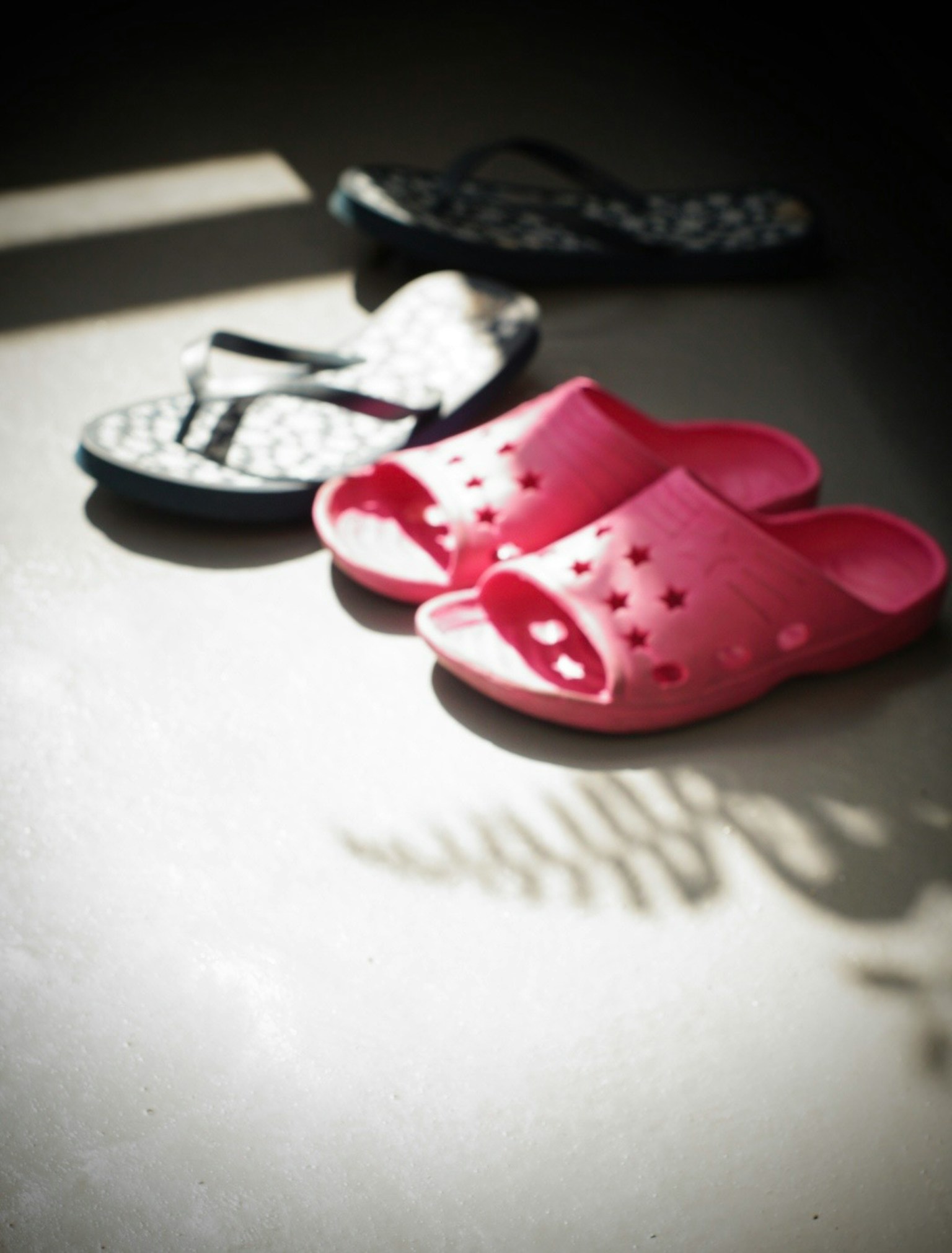 Red sandals and black flip-flops arranged on a shadowed floor