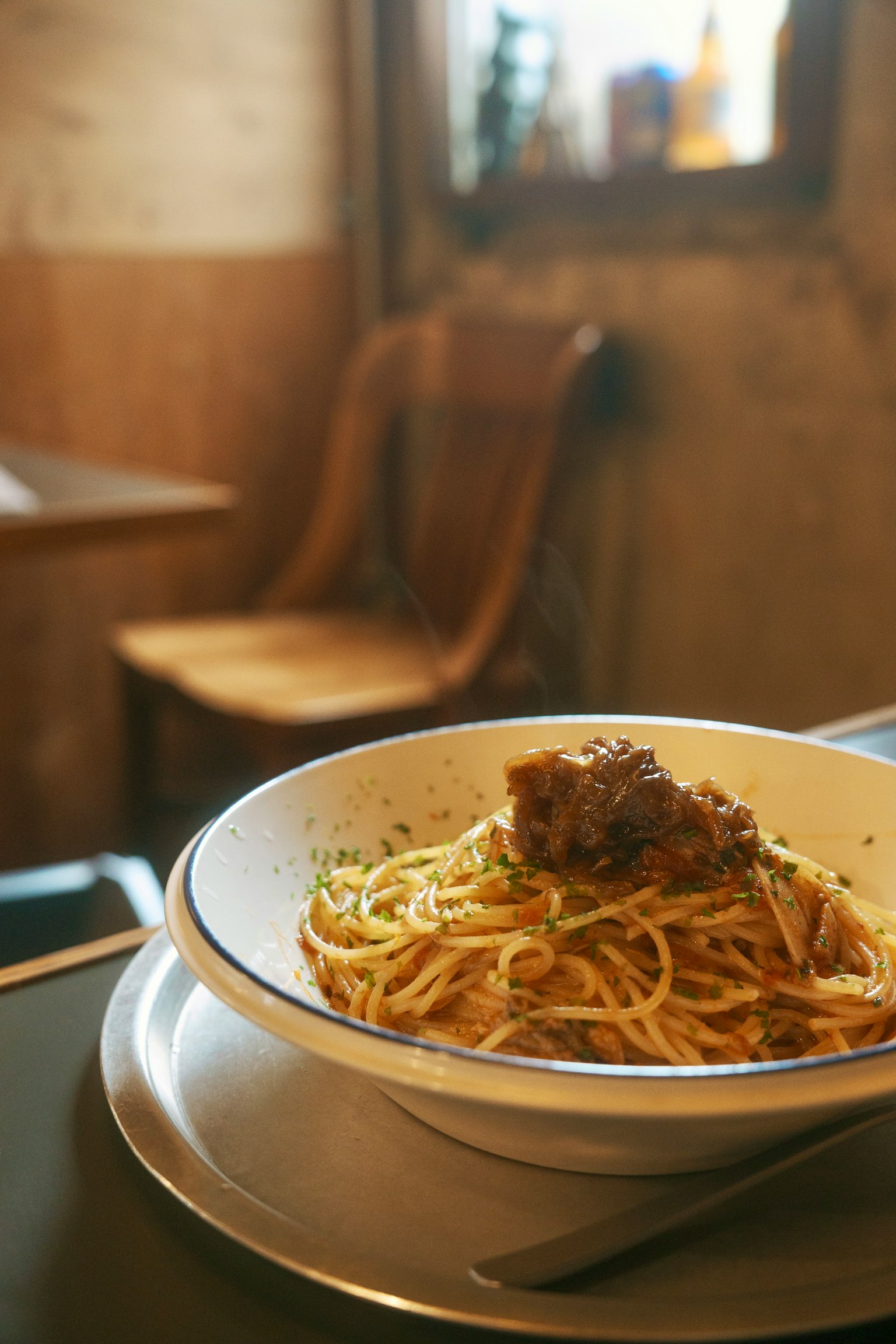 Eine Schüssel Spaghetti auf einem Teller mit einem Holzstuhl in einem Café