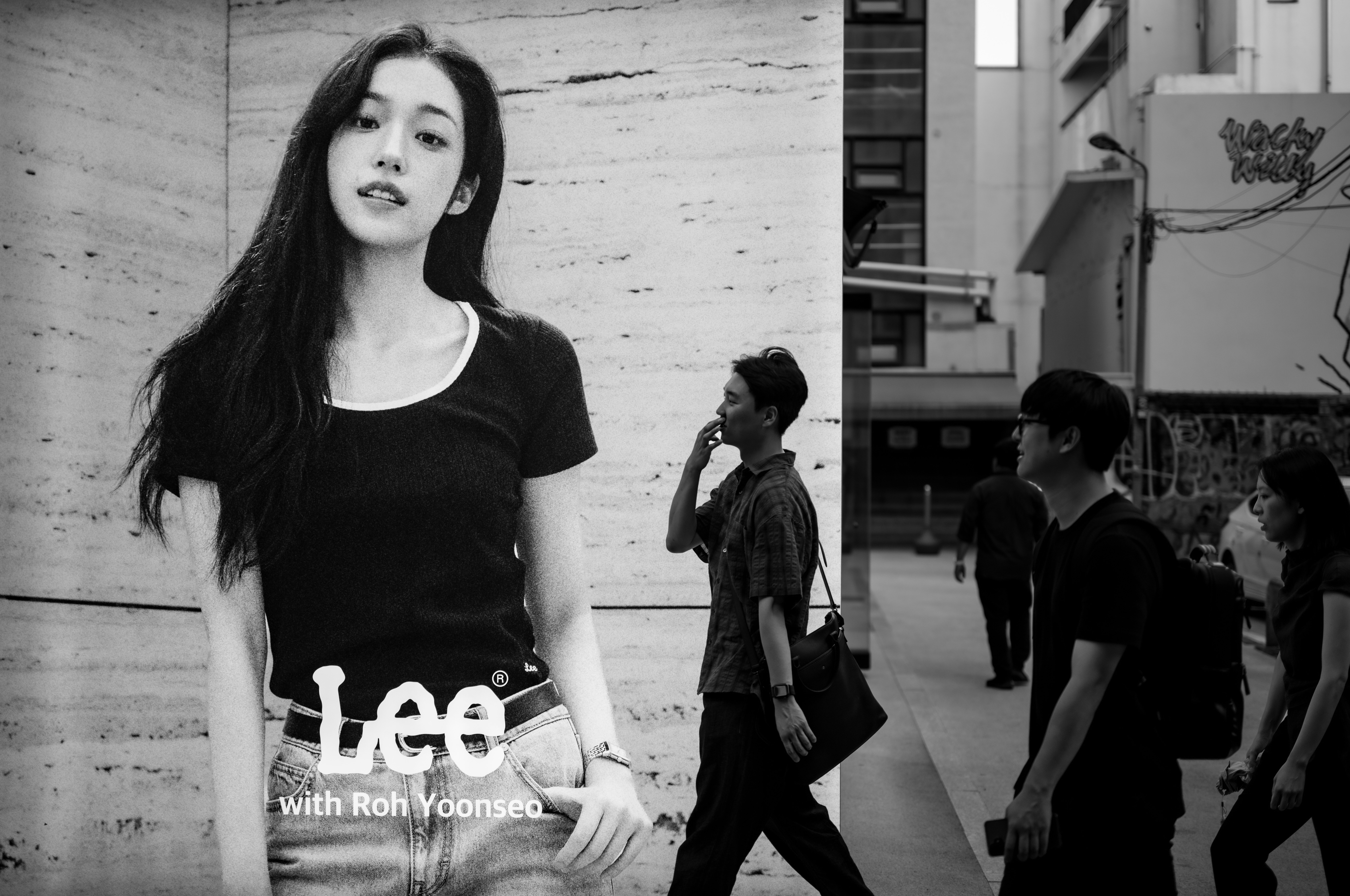 黒いTシャツの女性が路地で歩く人々の中に立つモノクロの街角