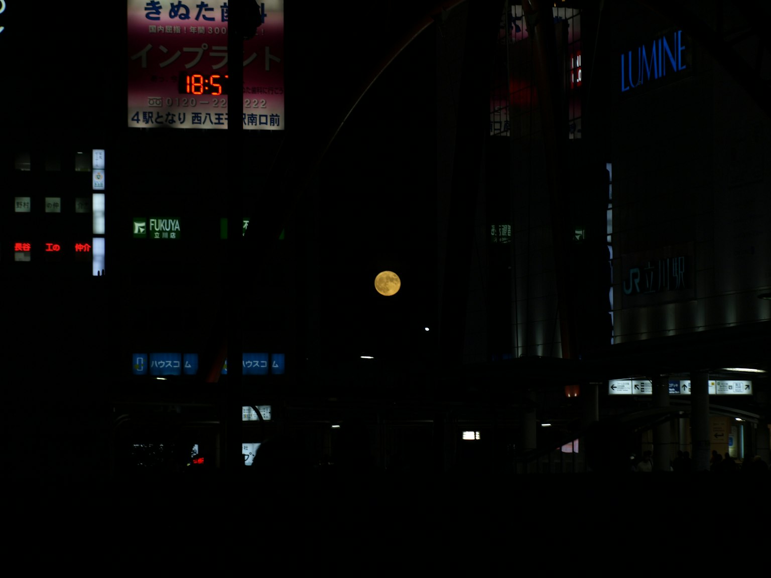 Full moon above a cityscape with neon signs at night