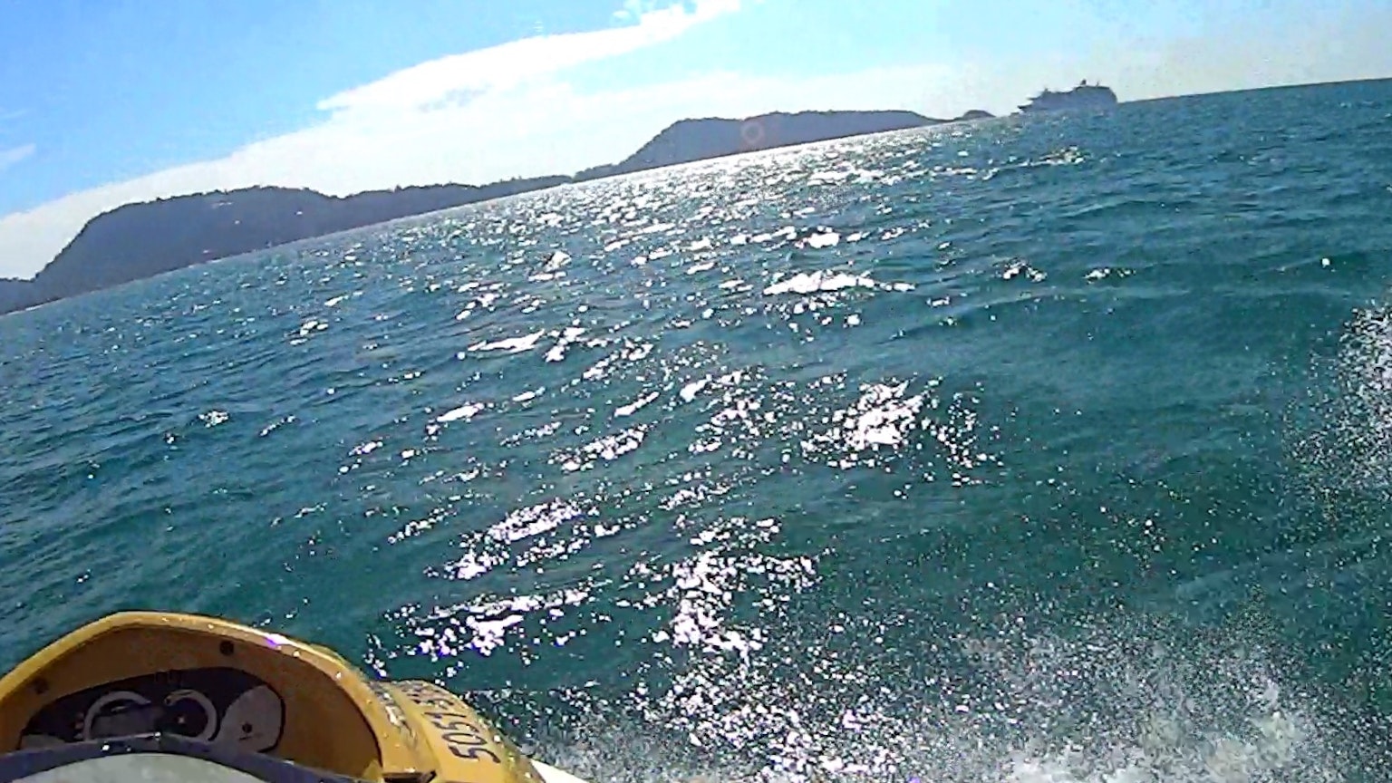 Jet ski menyemprot melalui ombak biru lautan dengan pulau-pulau di kejauhan
