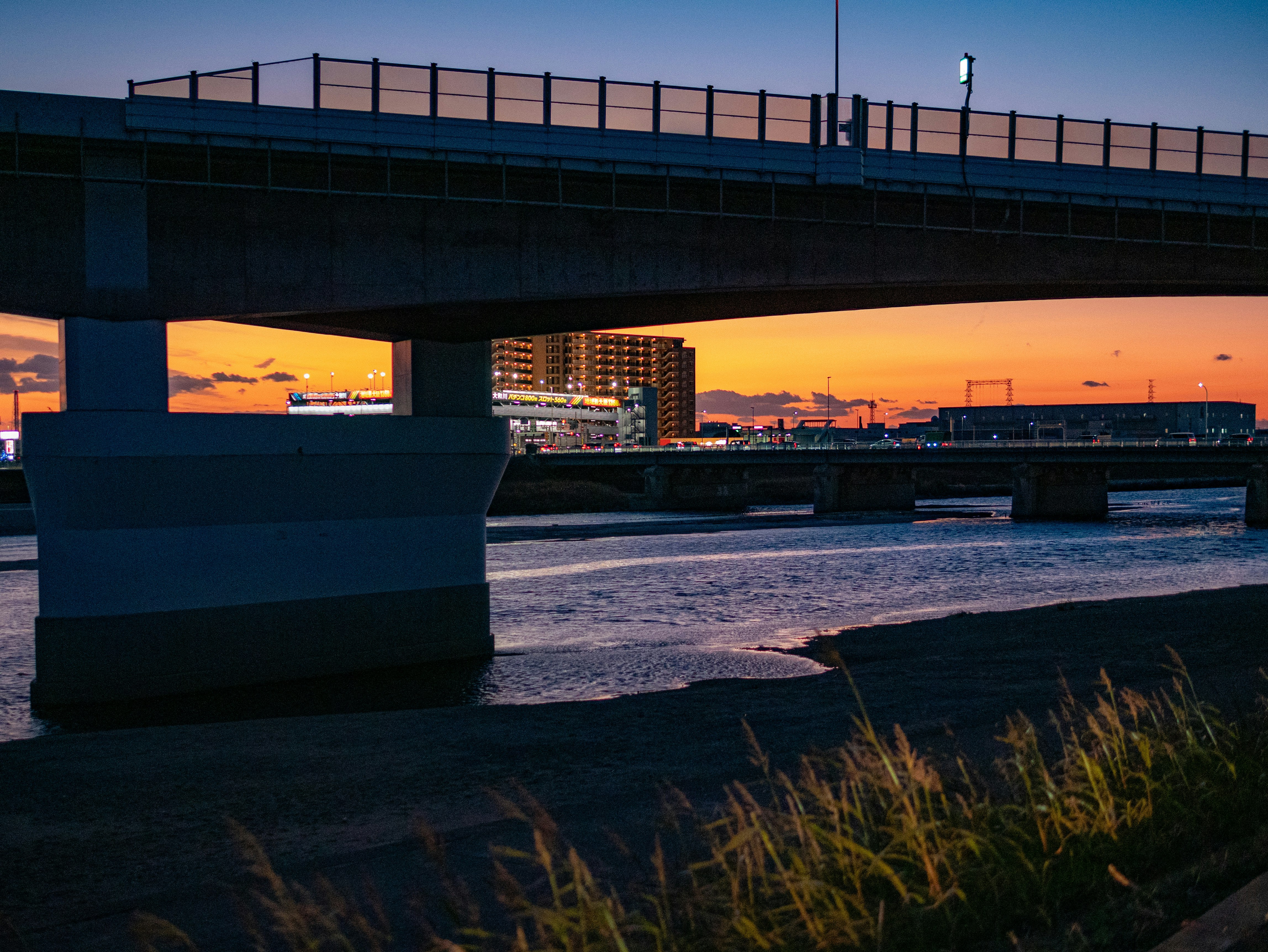 夕暮れの川沿いを走る高架橋と橋脚のある風景