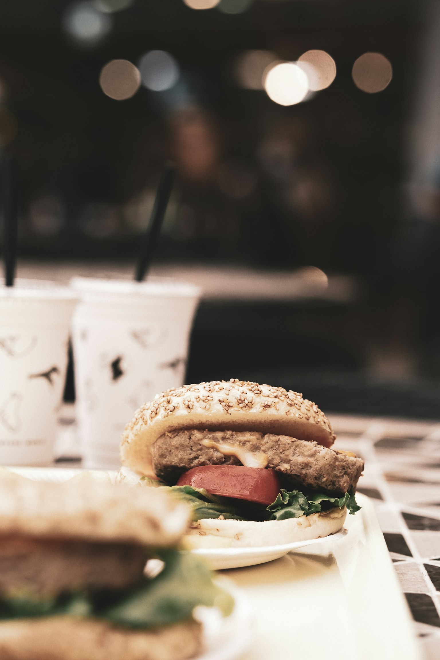 Hamburger dengan selada dan tomat di piring dengan dua minuman di latar belakang