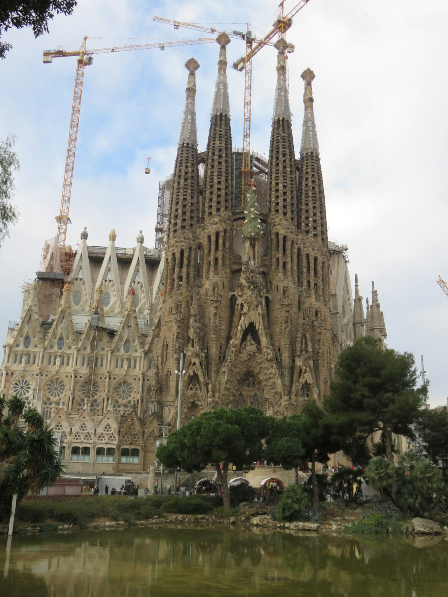 Sagrada Familia under construction featuring towers and cranes surrounded by greenery
