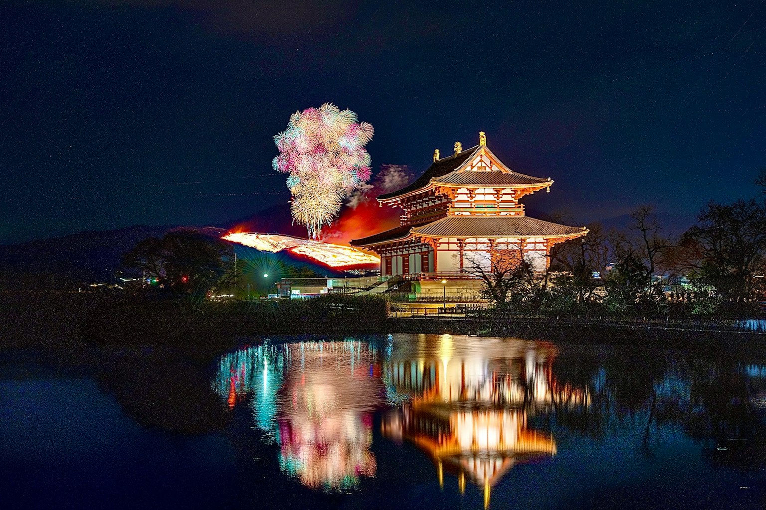 Un edificio tradizionale giapponese che si riflette su un lago di notte con fuochi d'artificio nel cielo