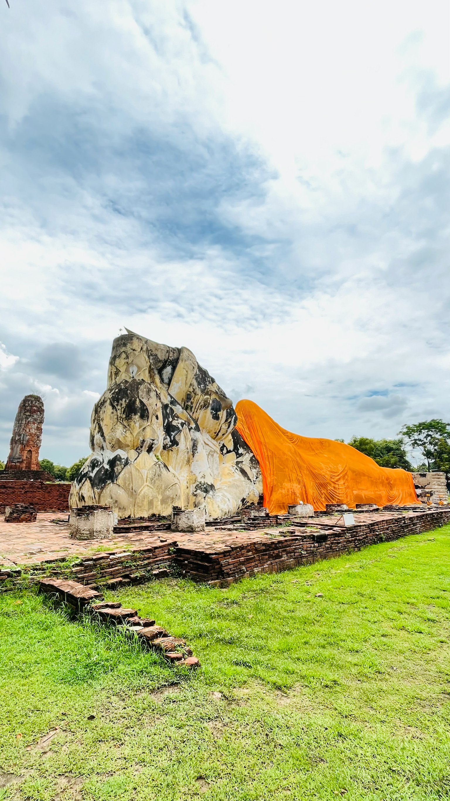 Grande statua del Buddha sdraiato ad Ayutthaya con antiche rovine e erba verde