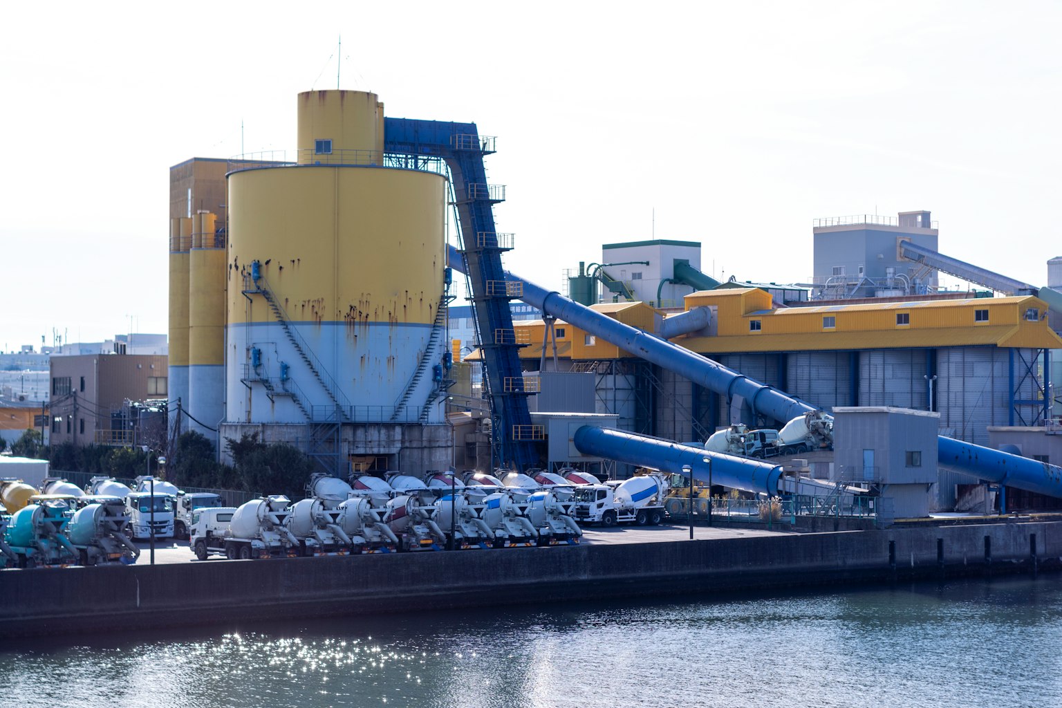 Industrial site featuring a yellow factory and concrete mixers by the water