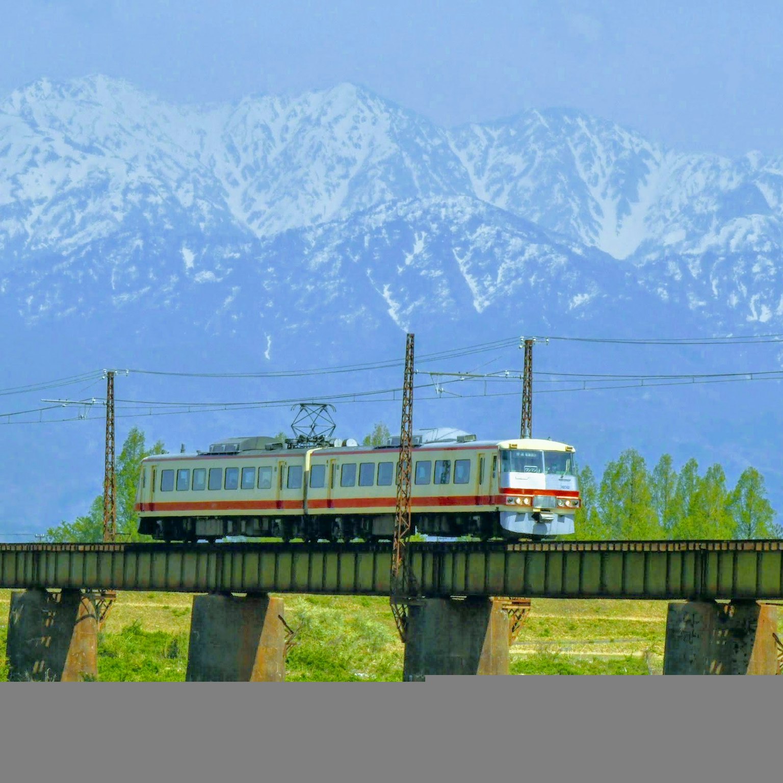 Kereta melintasi jembatan dengan latar belakang gunung bersalju