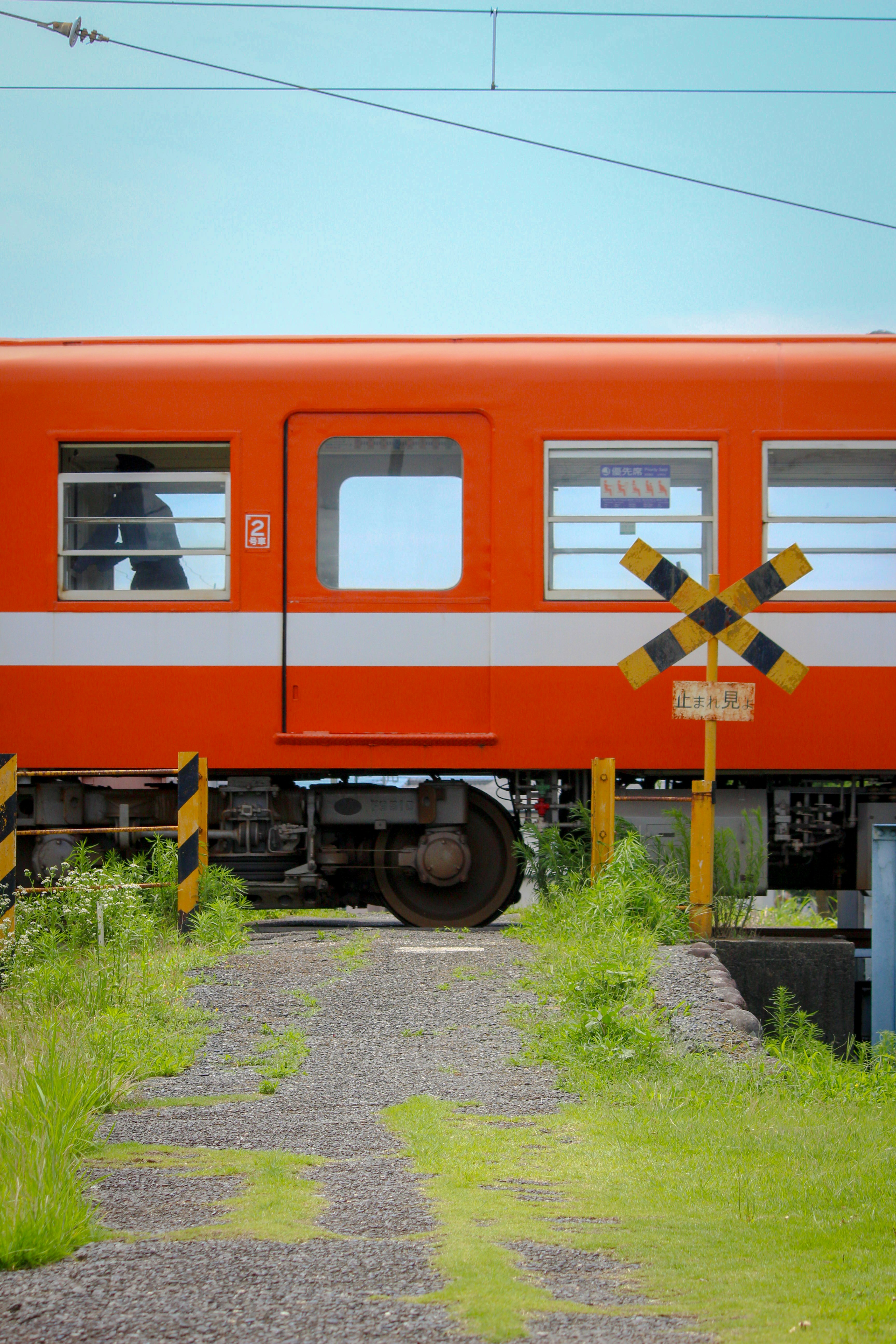 小さな踏切を通るオレンジのローカル列車