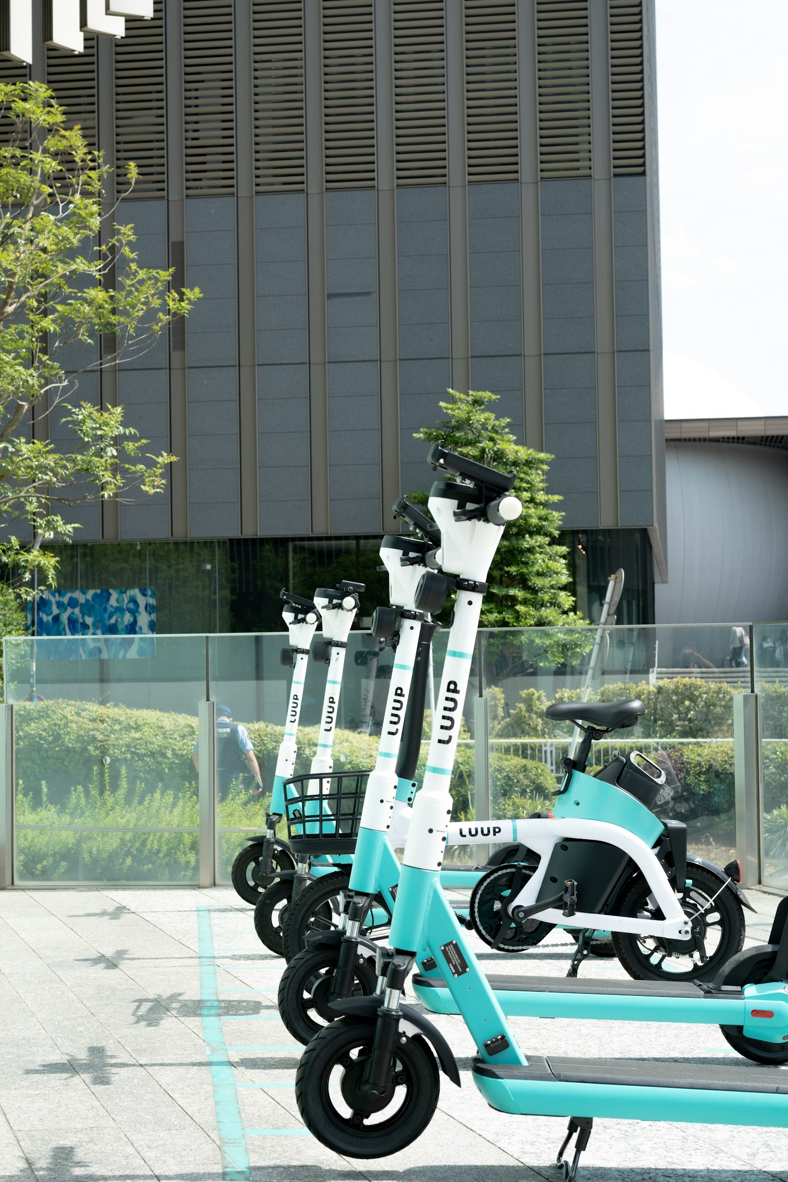 Rang de scooters électriques bleus et blancs dans un parking bâtiment moderne en arrière-plan