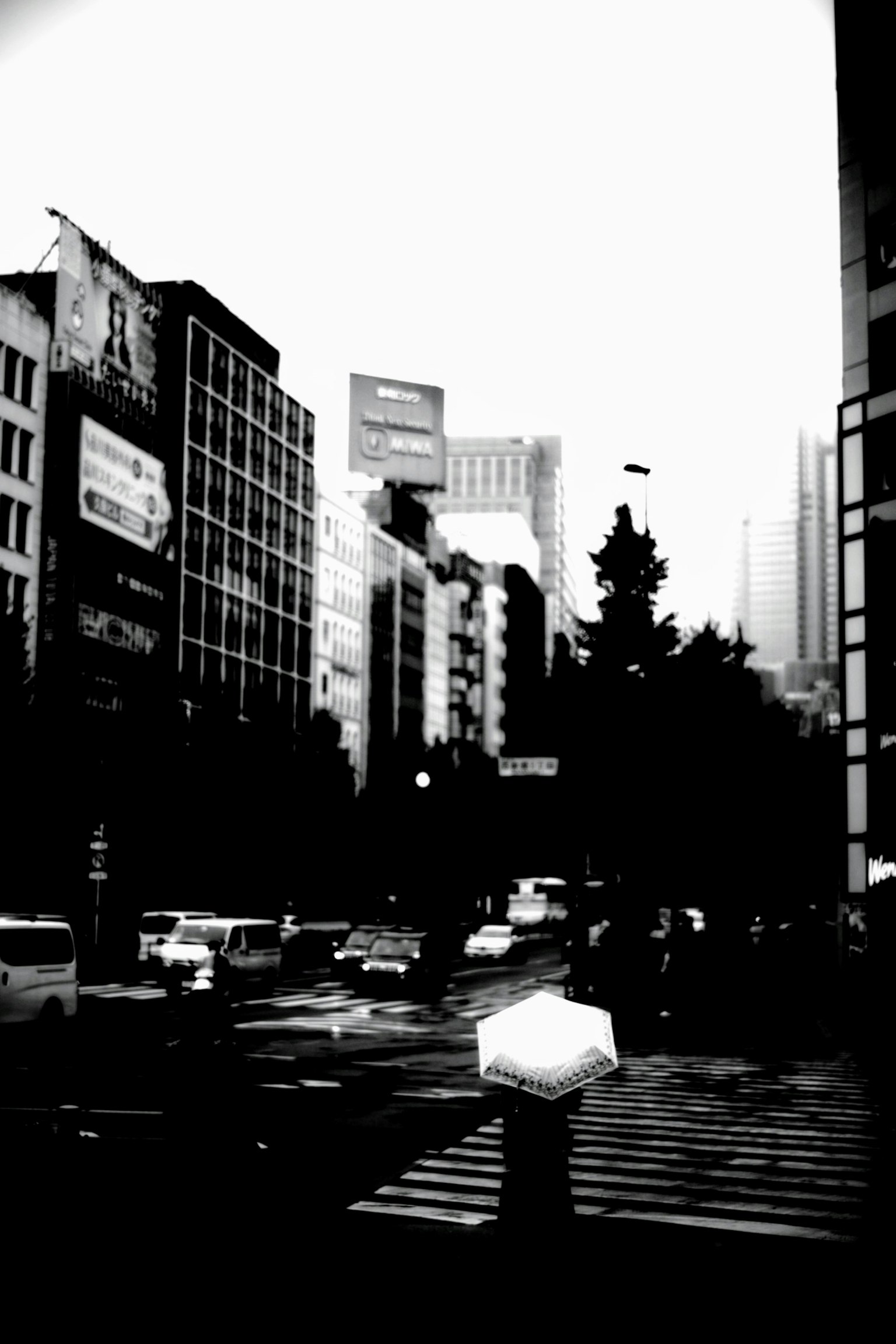 Black and white cityscape with buildings and cars on the street a person holding an umbrella in the rain