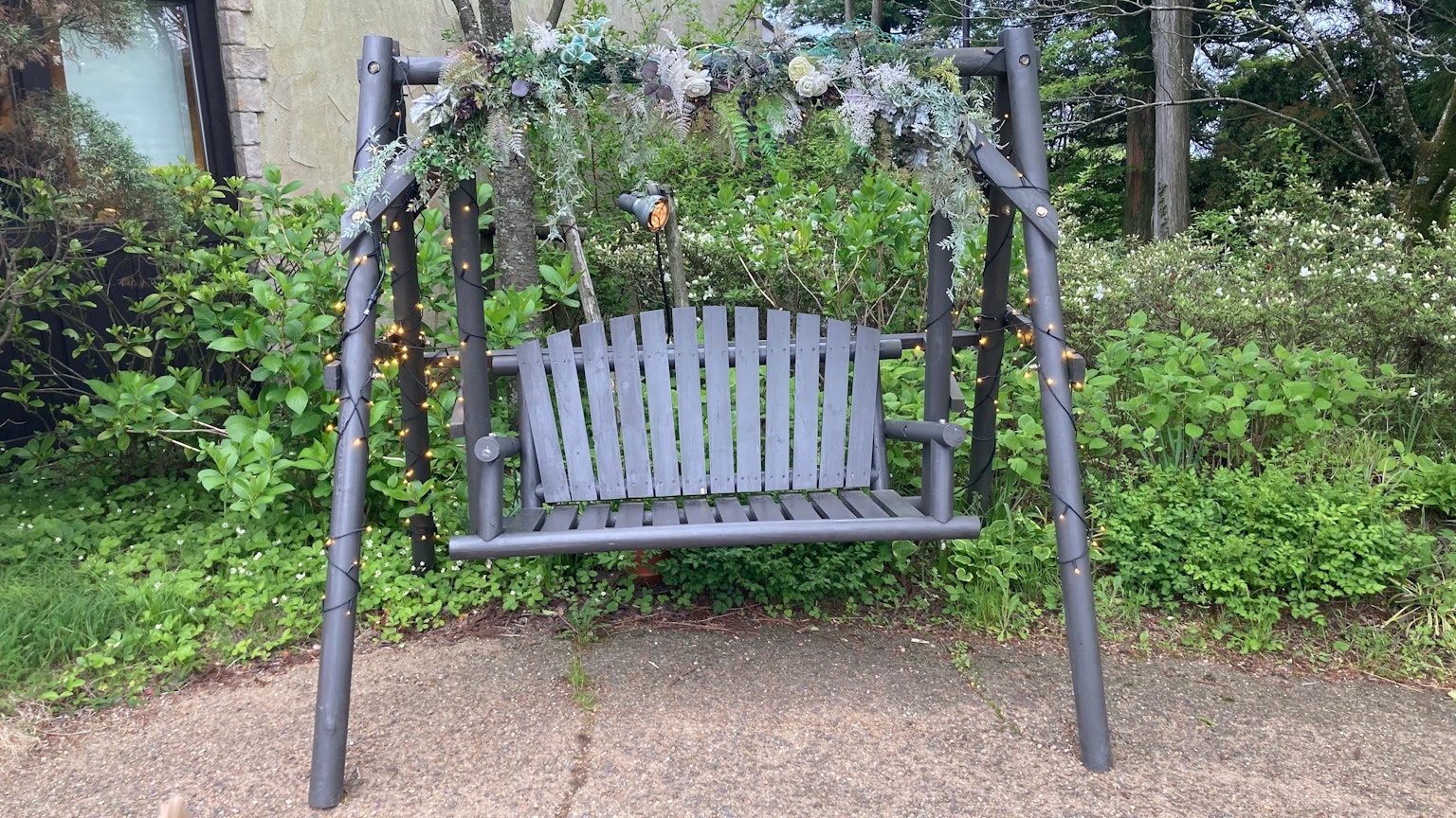 Balancelle en bois gris avec des décorations florales entourée de verdure
