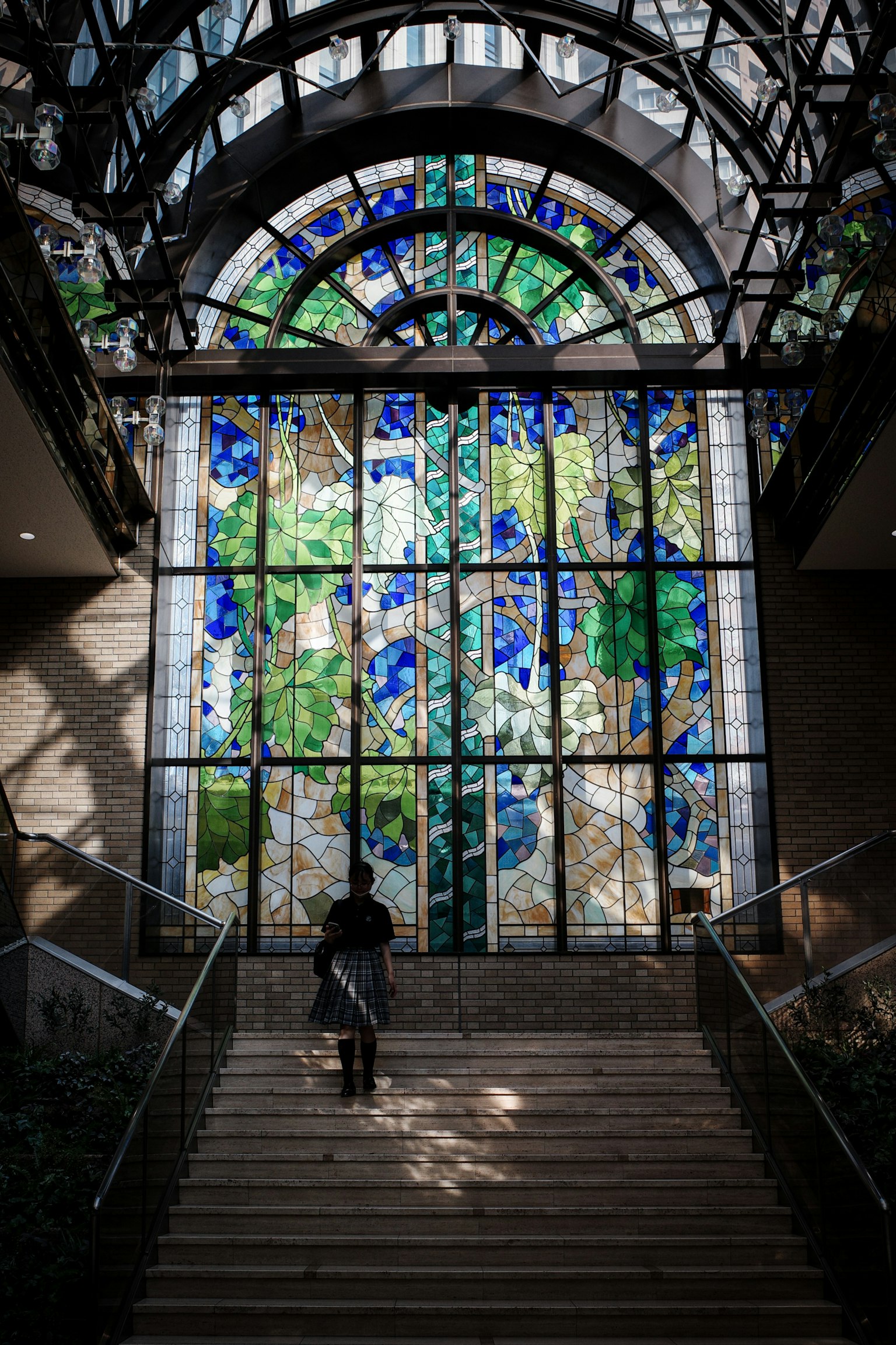 Pemandangan interior tangga dengan jendela kaca patri besar yang menampilkan warna-warna cerah dan desain rumit