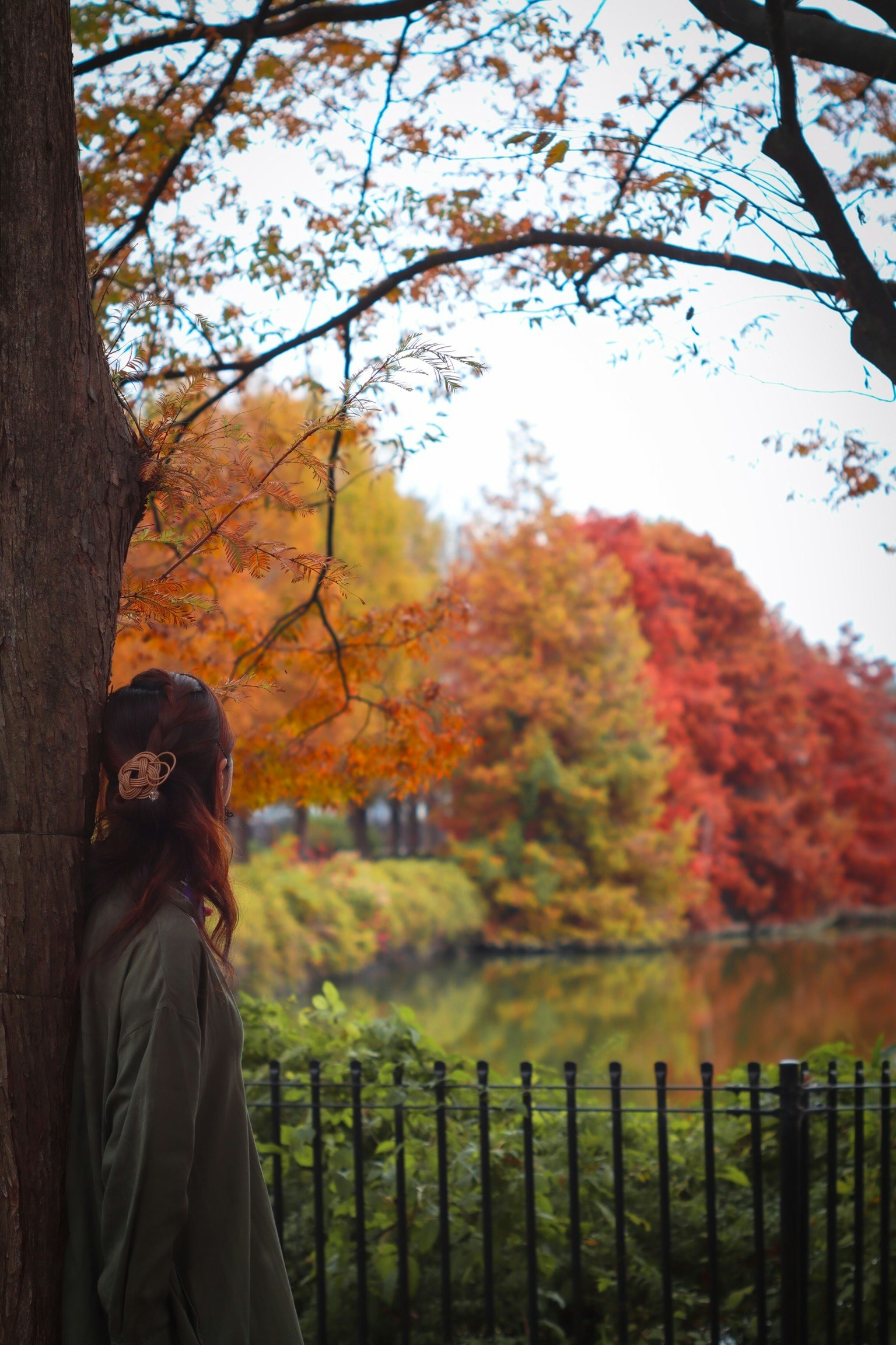 Frau lehnt an einem Baum in einem Park umgeben von herbstlichen Farben