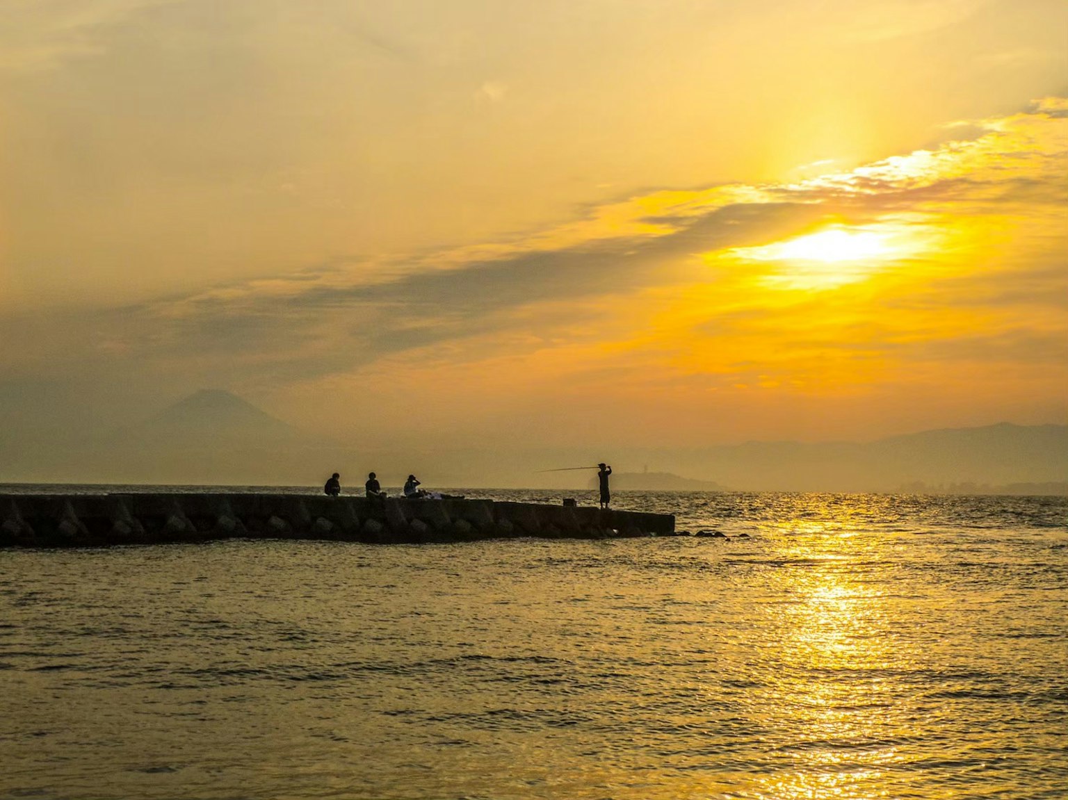 Scenic view of a sunset over the ocean with a pier and people standing