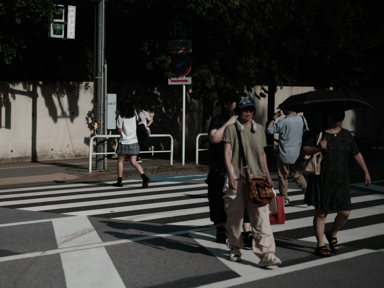 People crossing a crosswalk on a sunny day with a woman holding an umbrella and casually dressed individuals