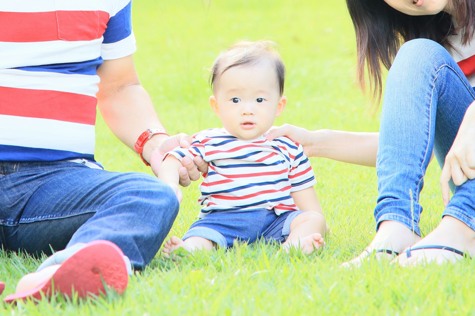 Eine Familie, die auf dem Gras sitzt, mit einem Baby in einem gestreiften Shirt