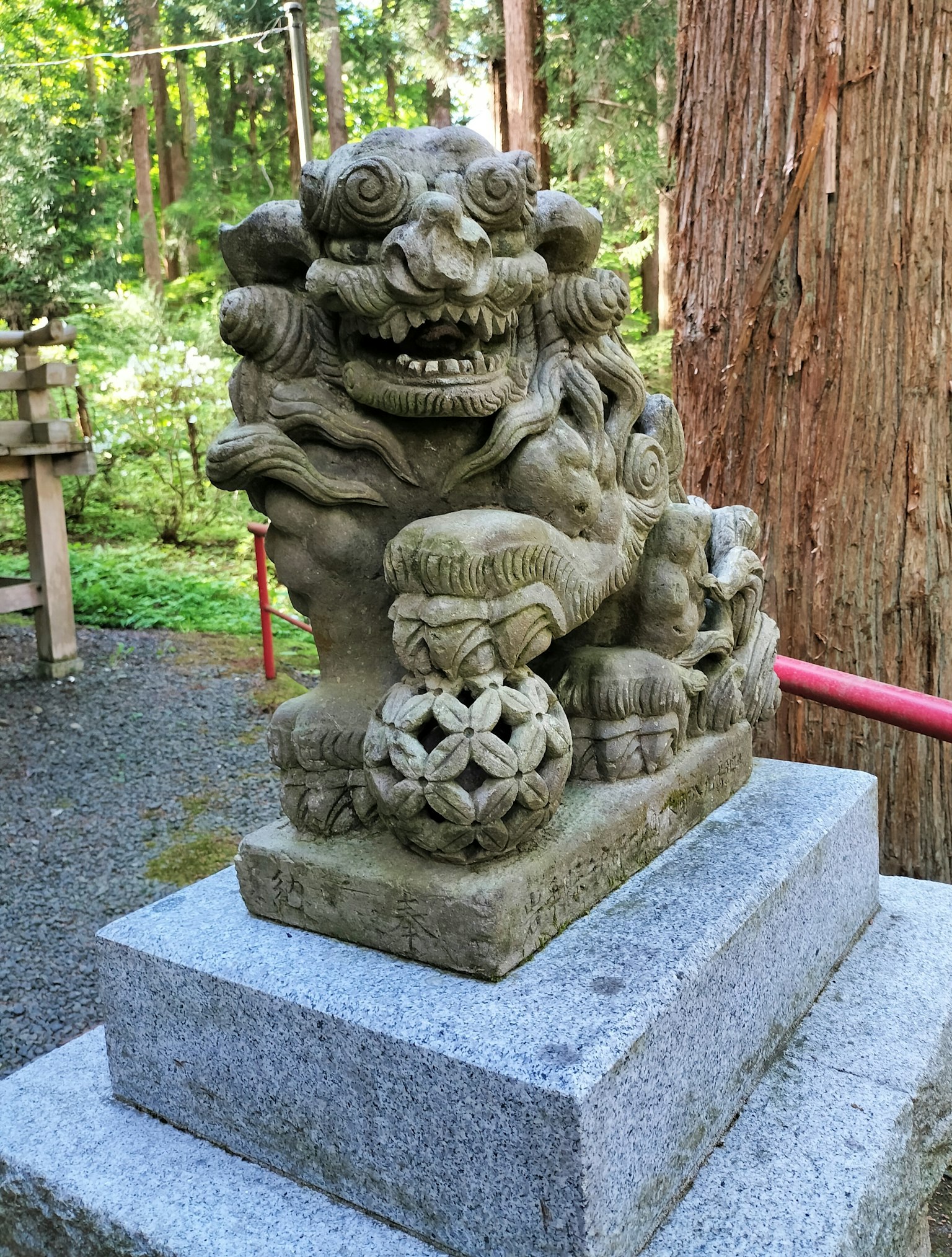 Lion gardien en pierre komainu assis sur un piédestal dans une forêt verte