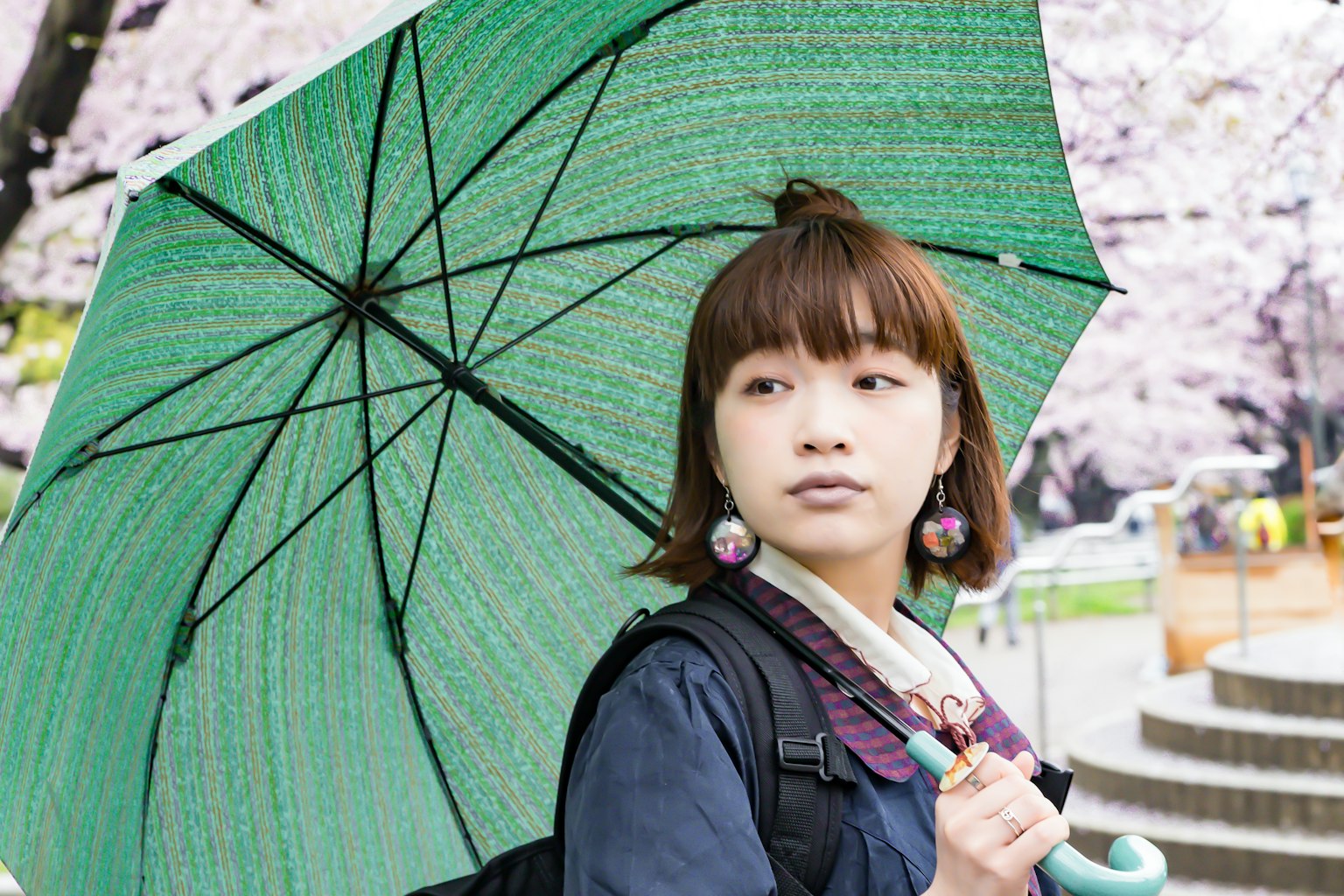 Portrait of a woman holding a green umbrella under cherry blossom trees