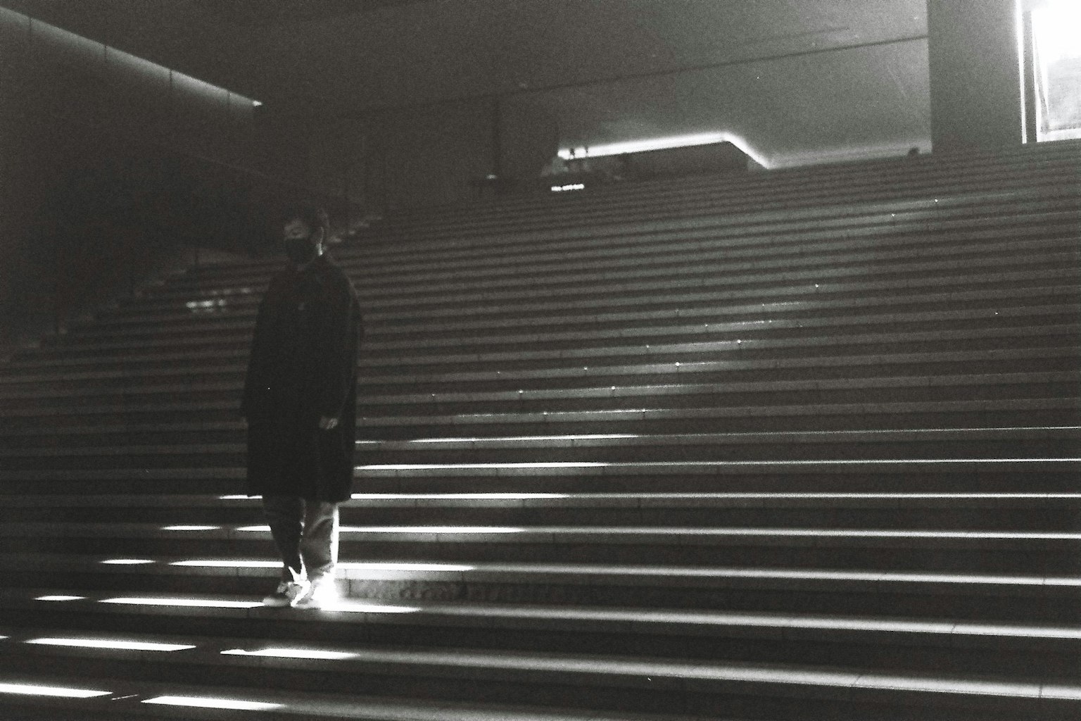 Imagen en blanco y negro de una figura subiendo escaleras con un contraste de luz impactante