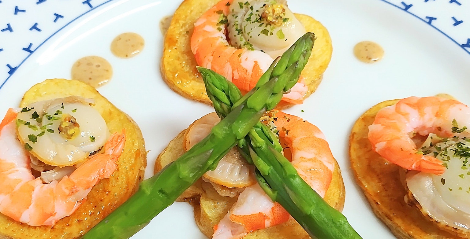 Entrée avec des crevettes et des pétoncles disposés sur une assiette avec des asperges croisées