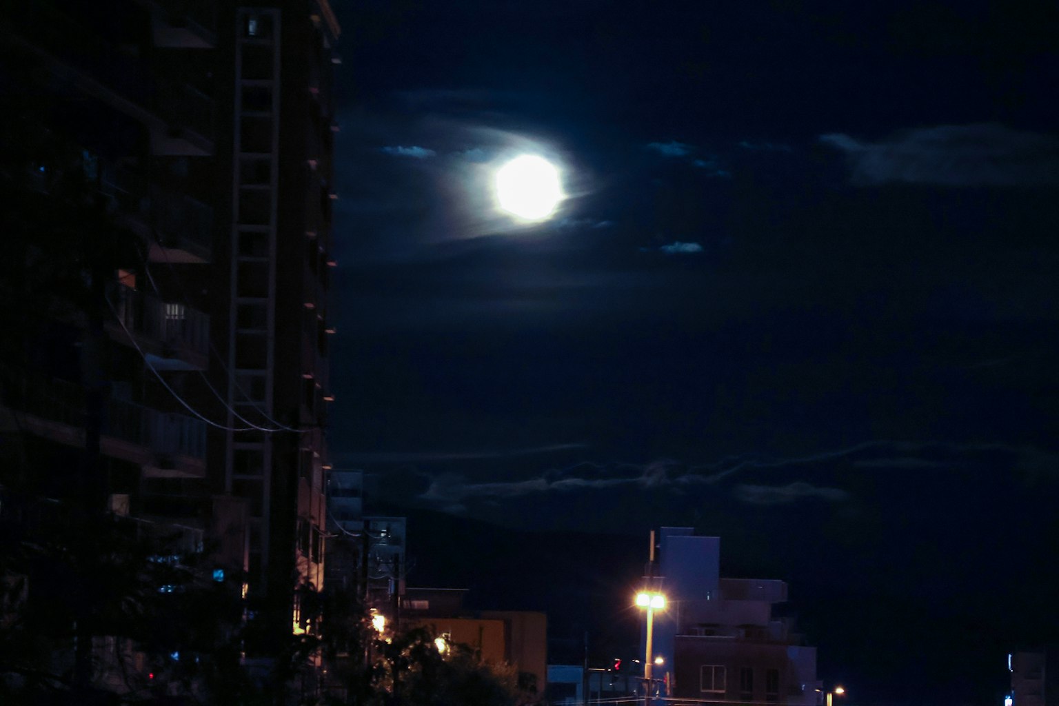 夜空中明亮的滿月和黑暗雲層下的城市景觀
