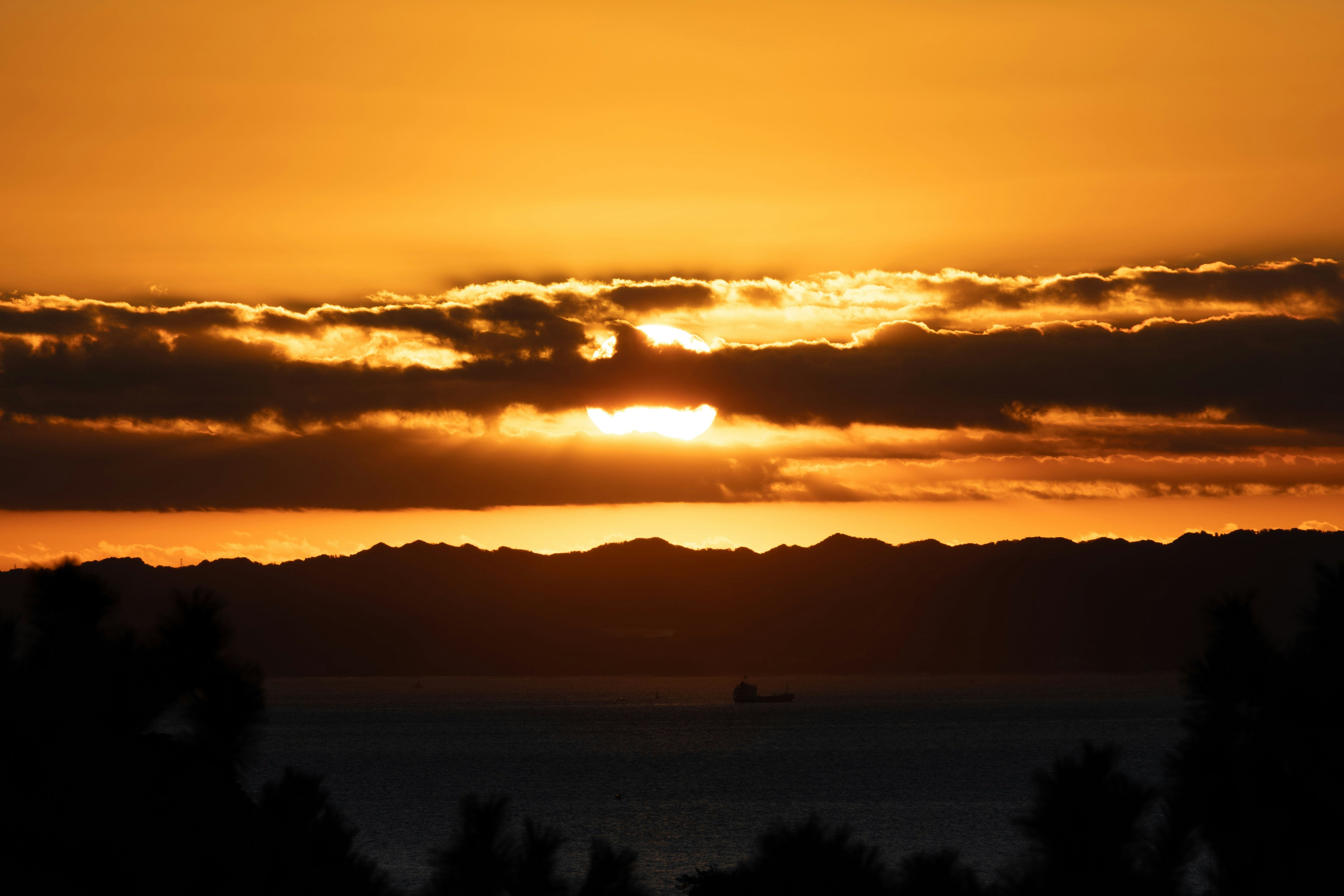 山並みと海に沈む夕日が雲の隙間から差し込む景色