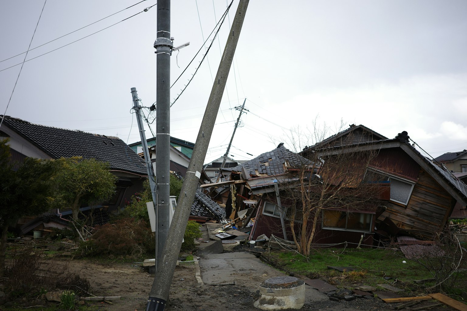 Escena de casas colapsadas y postes eléctricos inclinados
