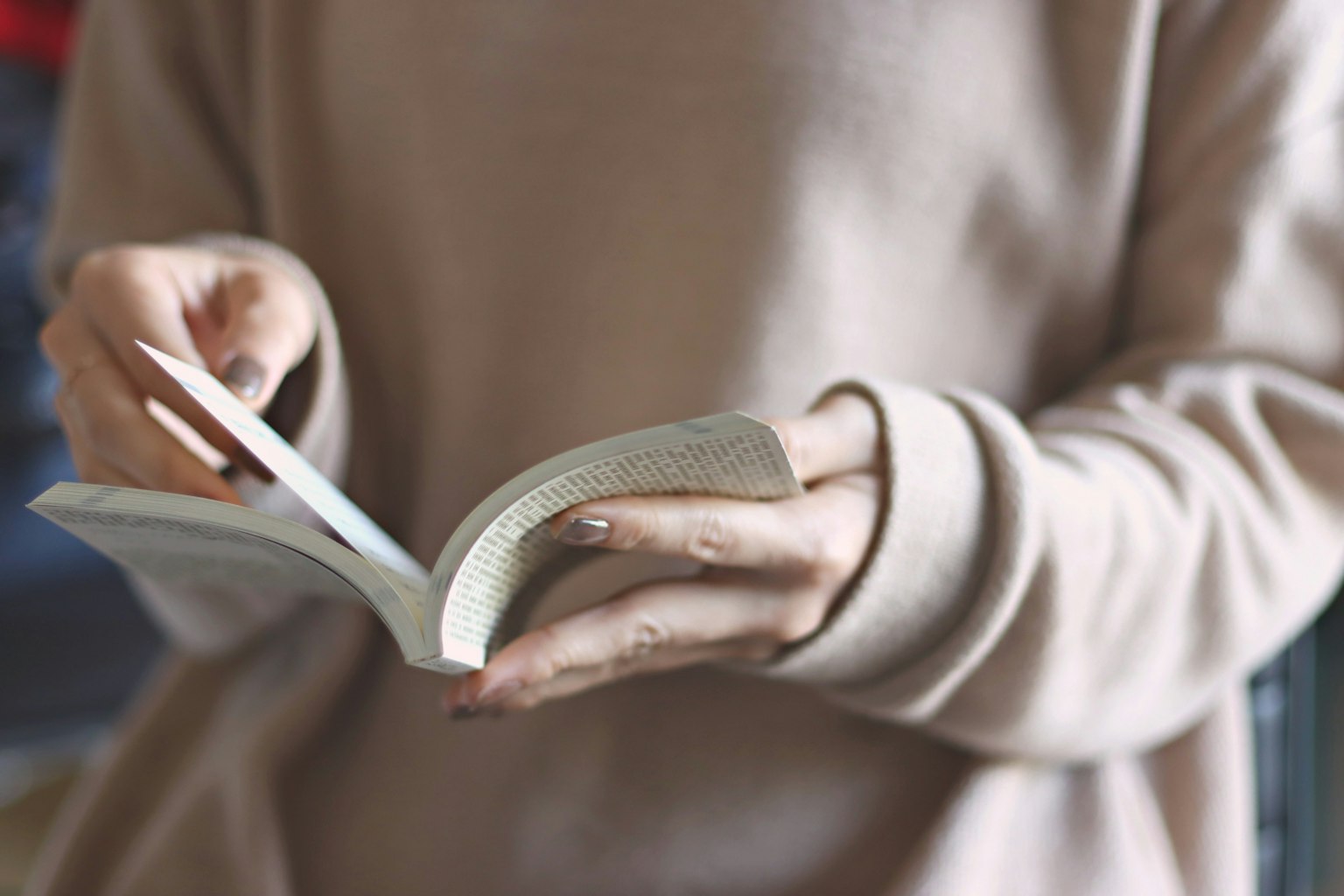 Close-up of a person holding a book wearing a soft-colored sweater