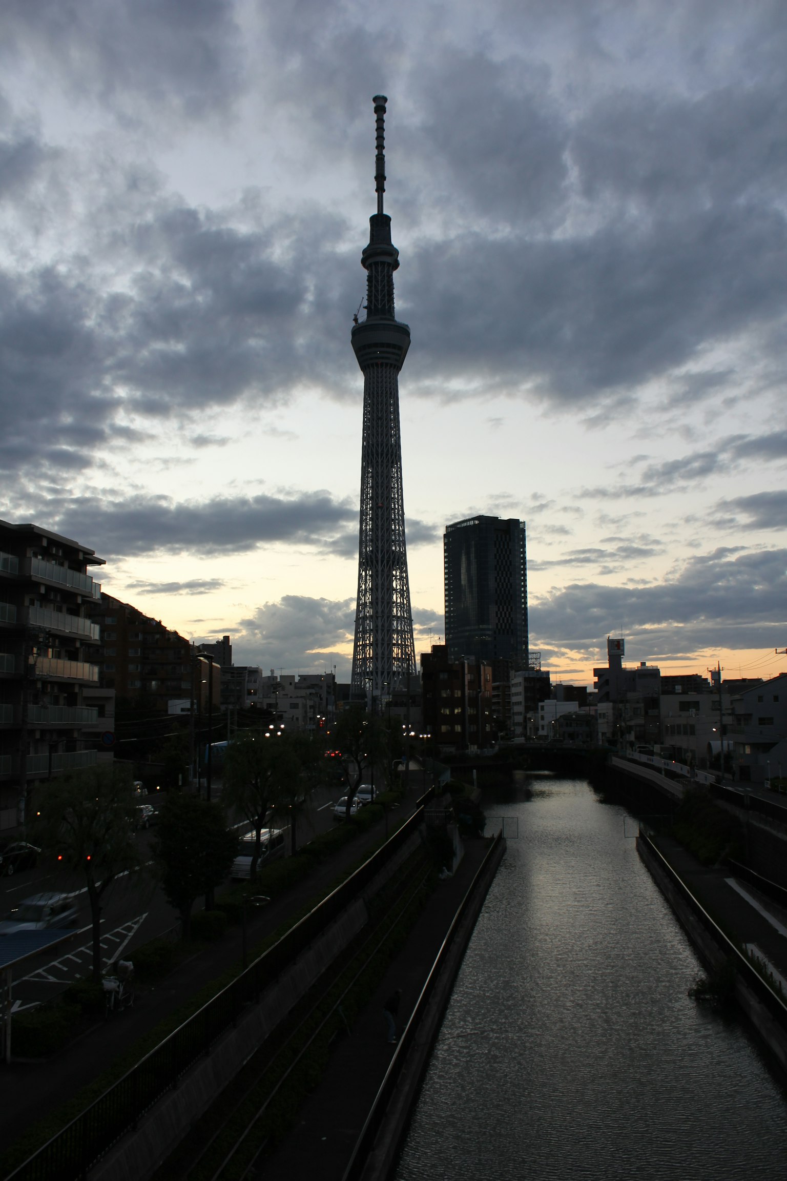 Tokyo Skytree silhouettiert vor einem dramatischen Abendhimmel mit Gebäuden und einem Fluss