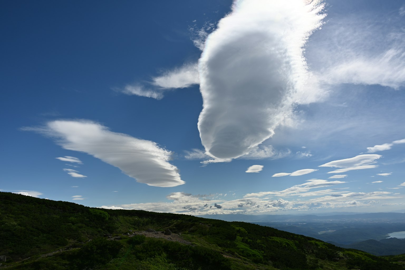 Awan unik mengapung di langit biru dengan bukit hijau