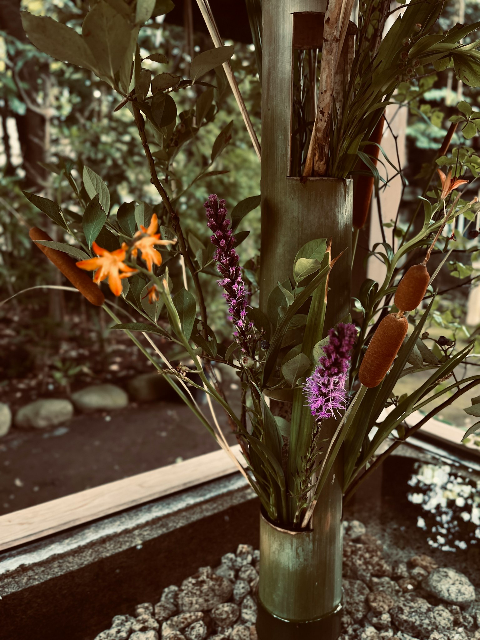 Bamboo vase with orange and purple flowers surrounded by lush greenery