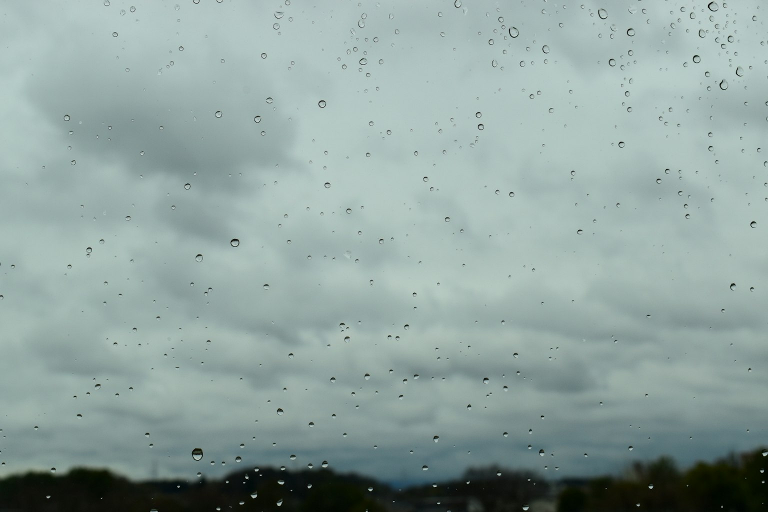Vista del cielo nuvoloso e delle montagne lontane attraverso una finestra bagnata dalla pioggia