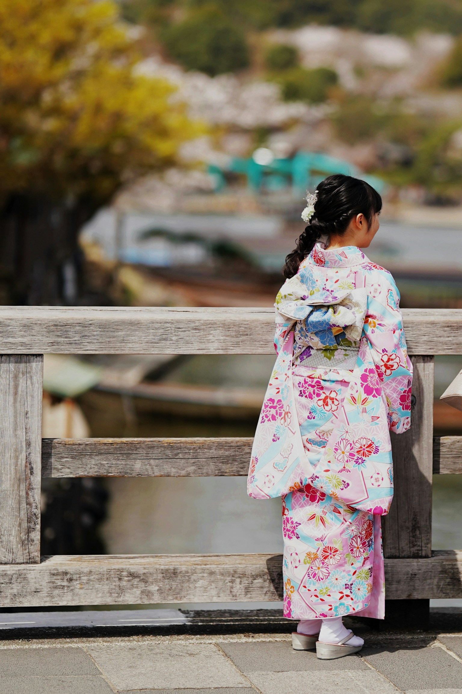 A girl in a beautiful floral kimono stands on a bridge