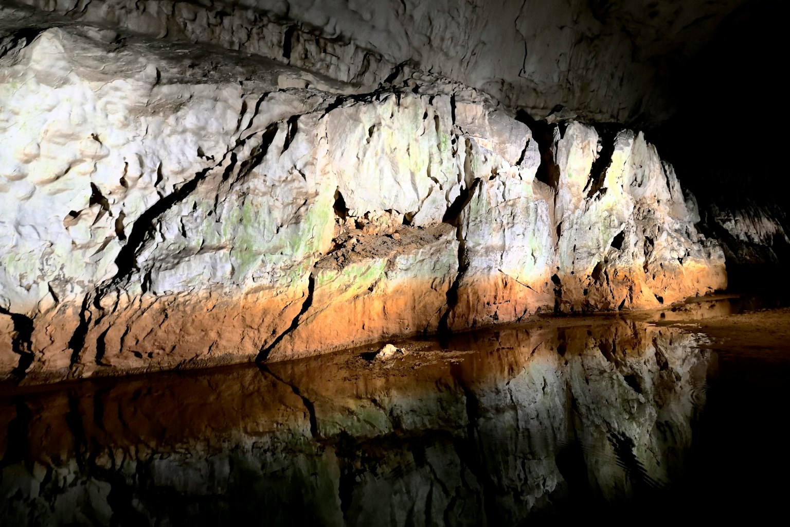 Beleuchtete Höhlenwand mit Reflexionen auf der Wasseroberfläche