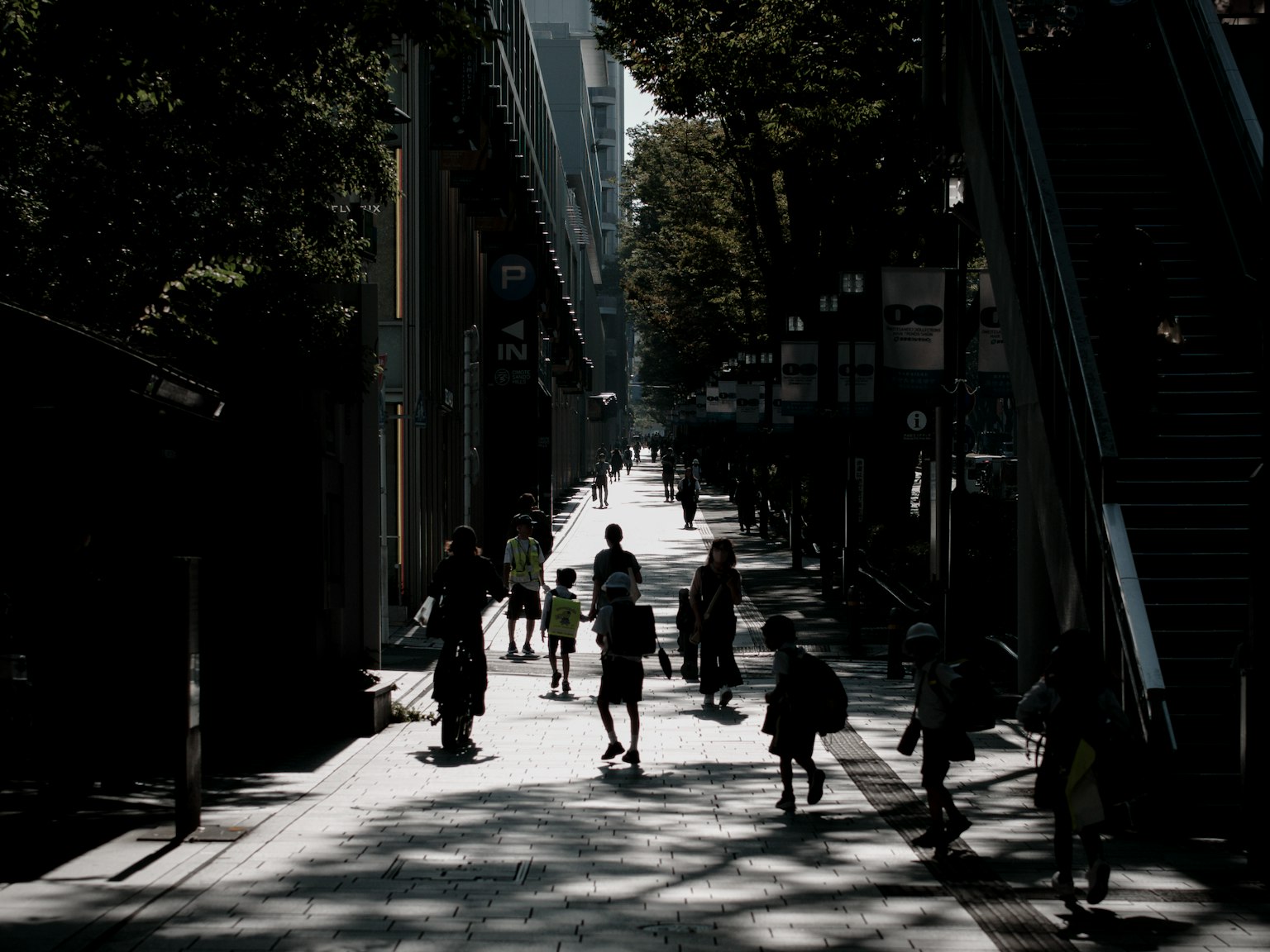 Menschen gehen in einer schattigen Straße mit Silhouetten von Bäumen