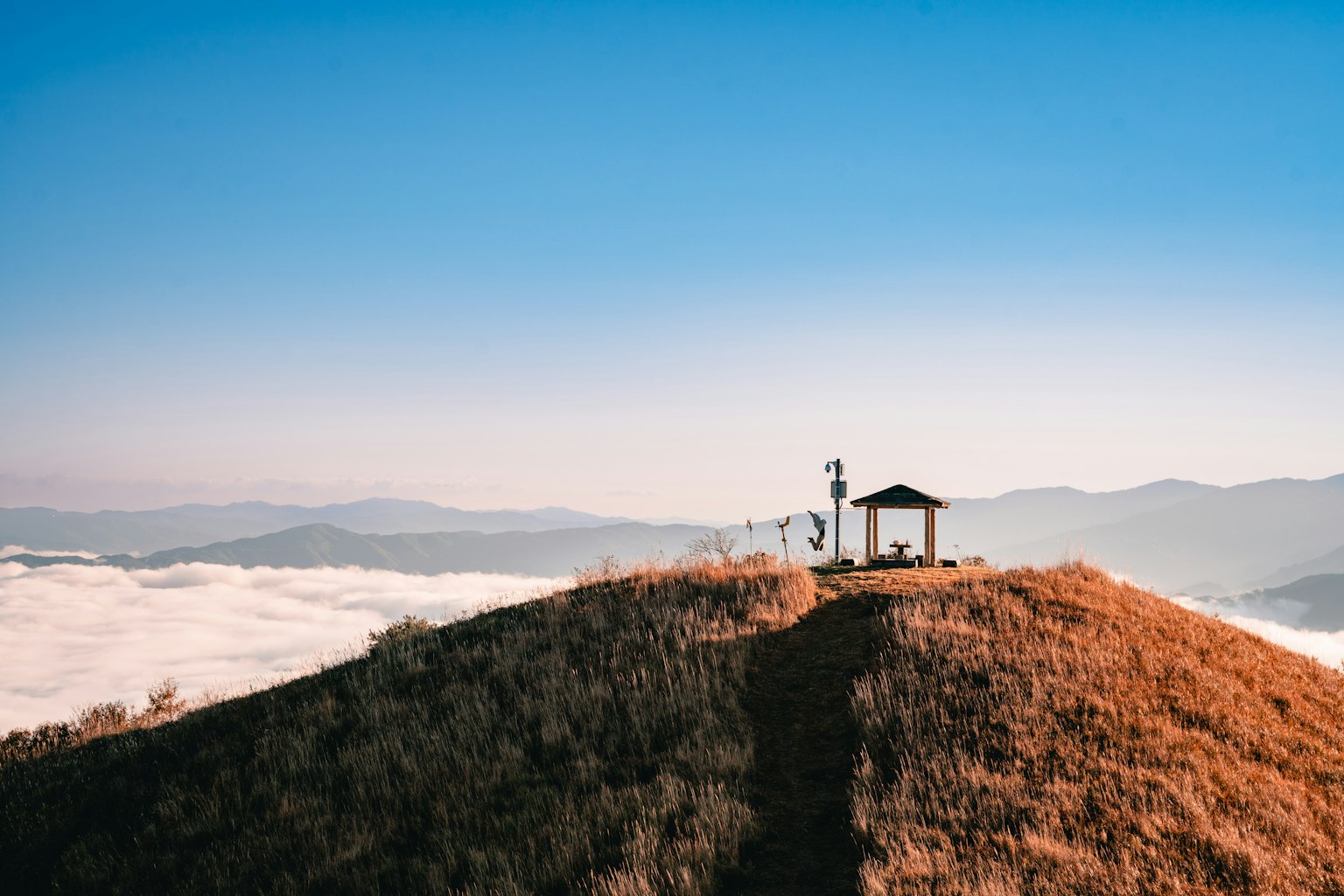Un petit gazebo sur une colline herbeuse au-dessus des nuages
