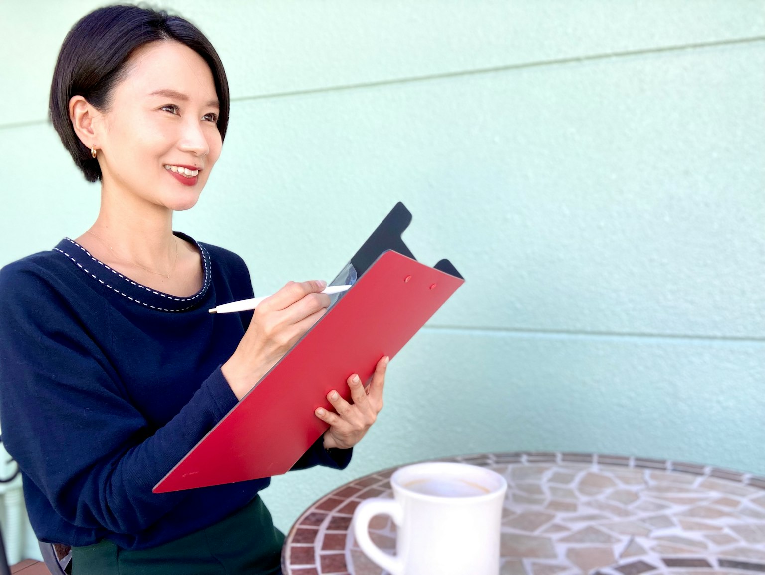 Une femme souriante tenant un clipboard rouge et écrivant avec un stylo