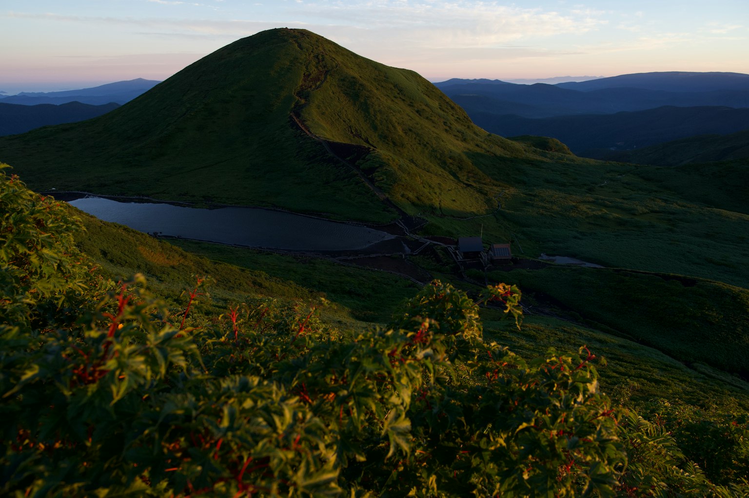 绿色山丘与宁静湖泊在夕阳光照耀下的景色