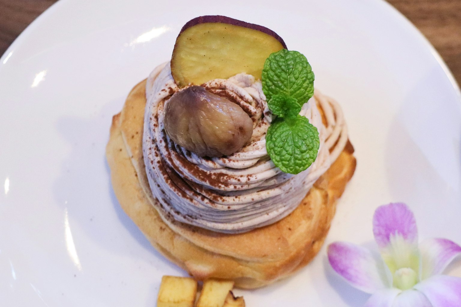 Postre con crema y castañas decorado con menta y una flor púrpura
