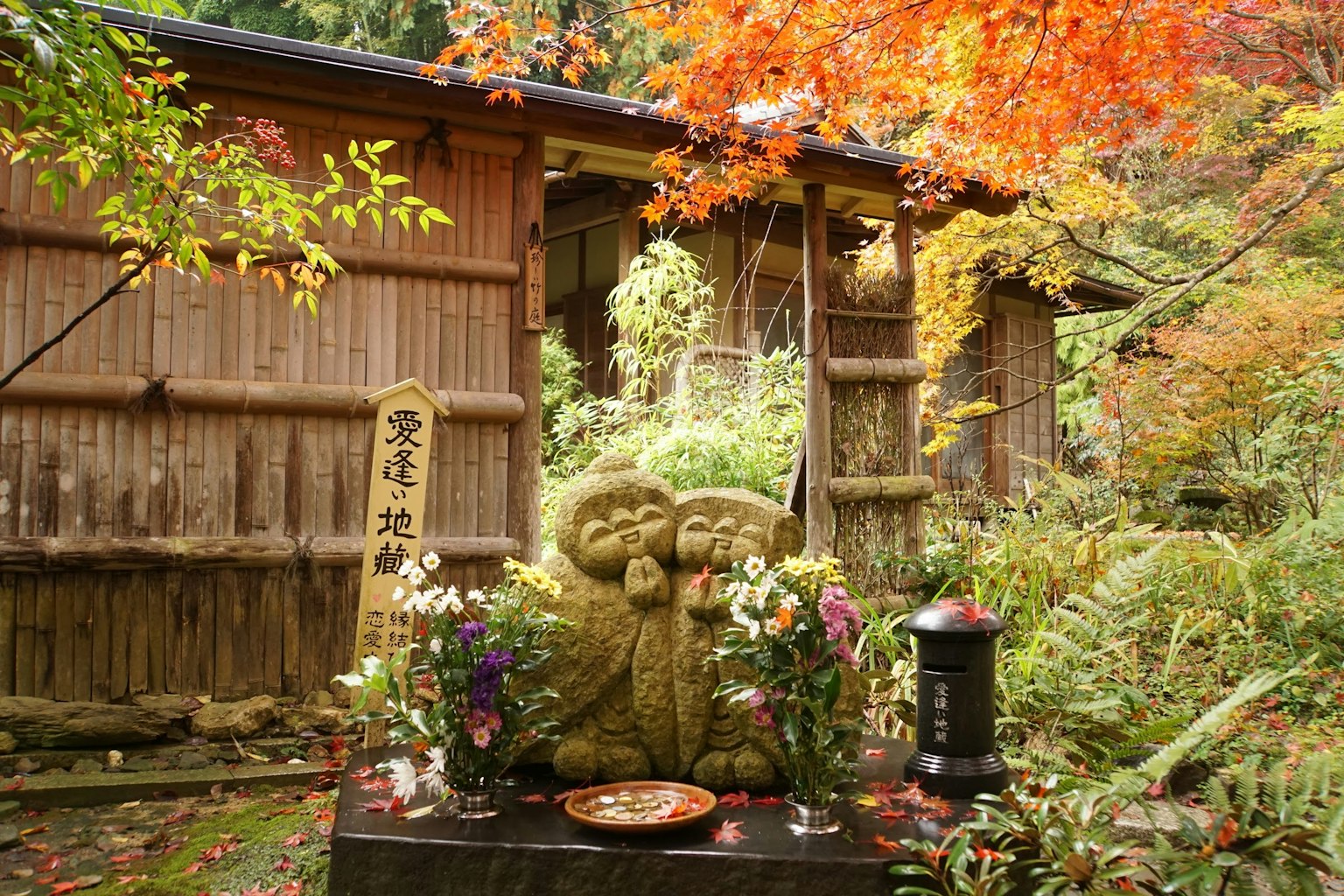 Steinskulptur umgeben von herbstlichem Laub und geschmückt mit Blumen
