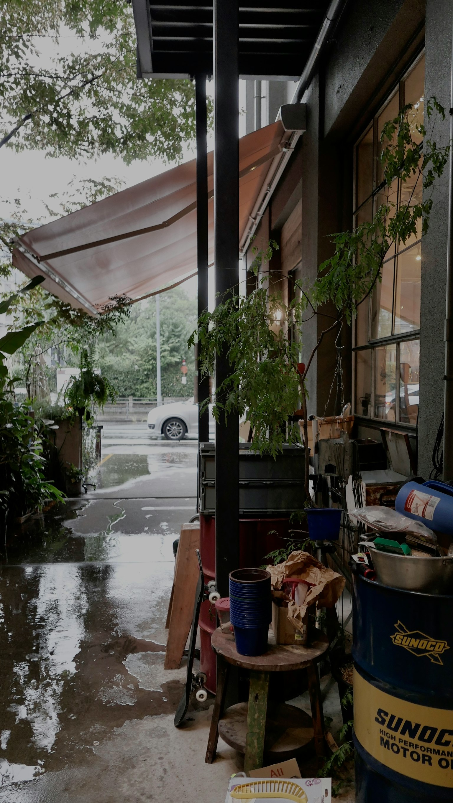 雨の中のカフェの外観 植物と色とりどりの容器が並ぶ
